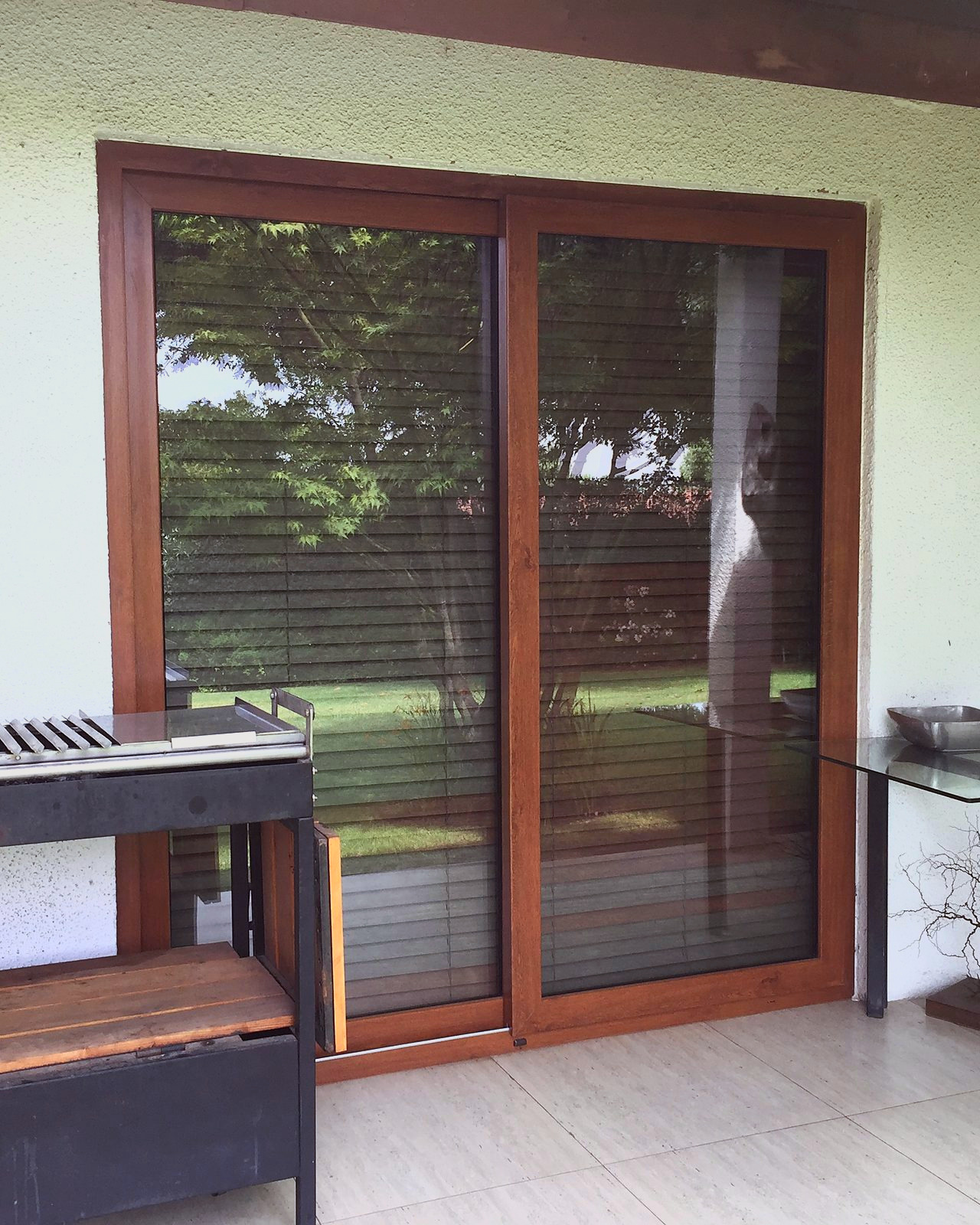 Puerta corredera de dos hojas, de PVC foliado imitación nogal, que abre a una terraza techada con piso cerámico. Es PVC foliado imitación madera, no es madera.