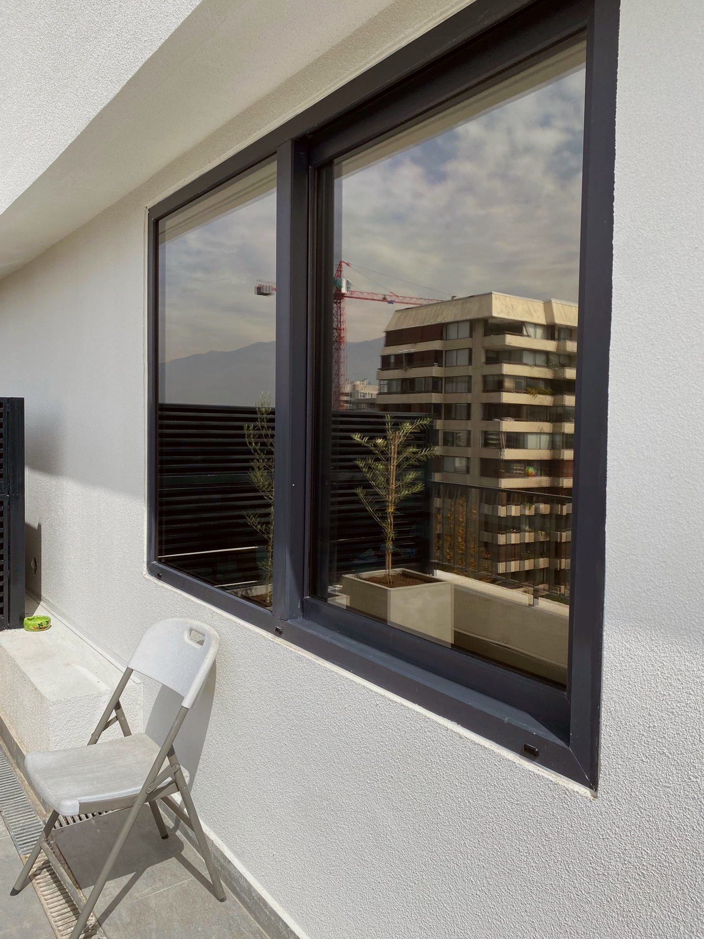 Ventana de dos hojas con perfiles de PVC antracita, en la terraza de un departamento, con plantas junto al muro.