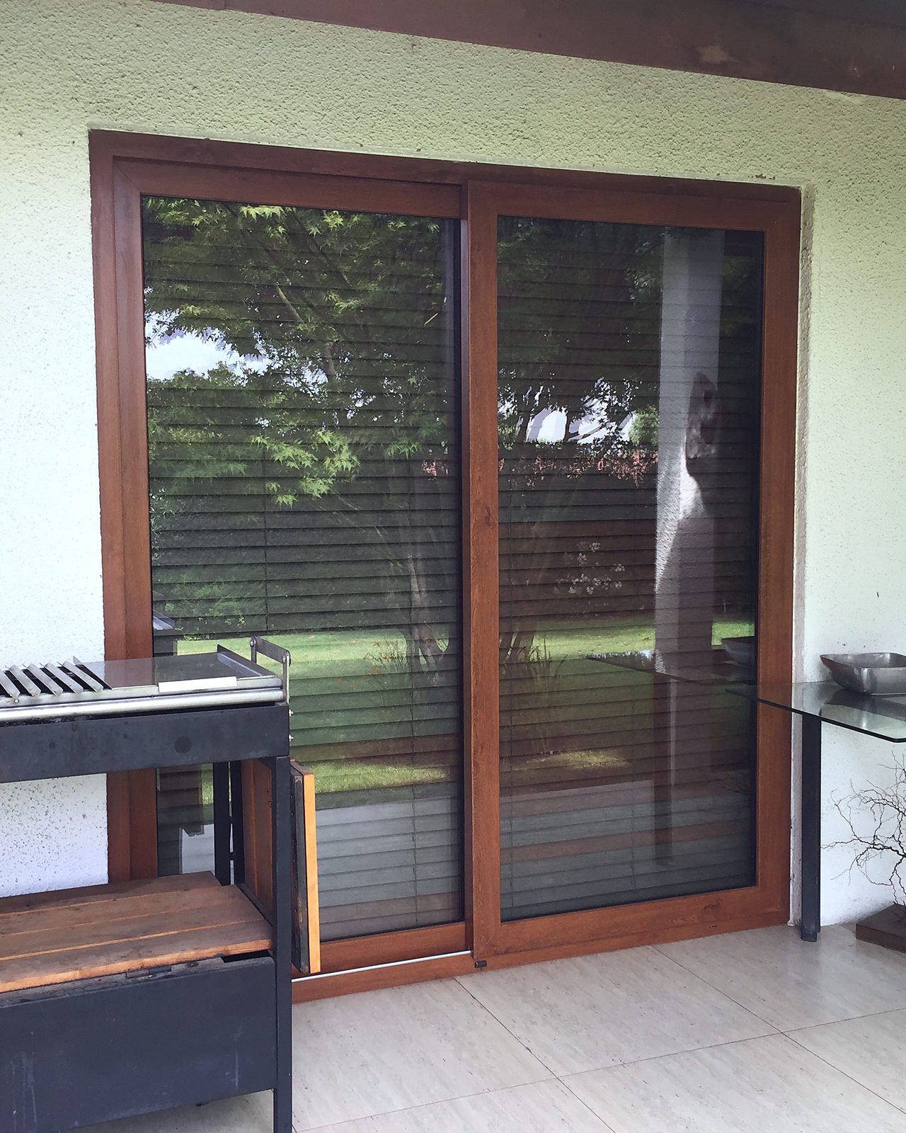 Puerta corredera de PVC foliado imitación madera nogal, de dos hojas, que da a una terraza techada con piso cerámico. No es madera.